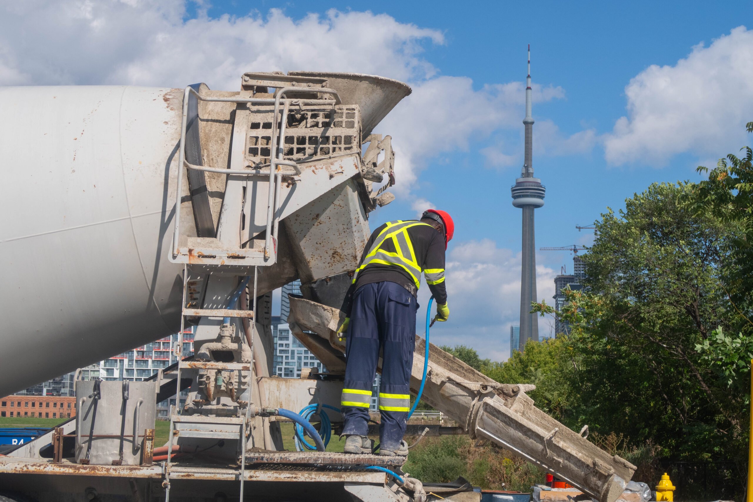 Construction worker cleaning cement truck in front of Toronto CN Tower.